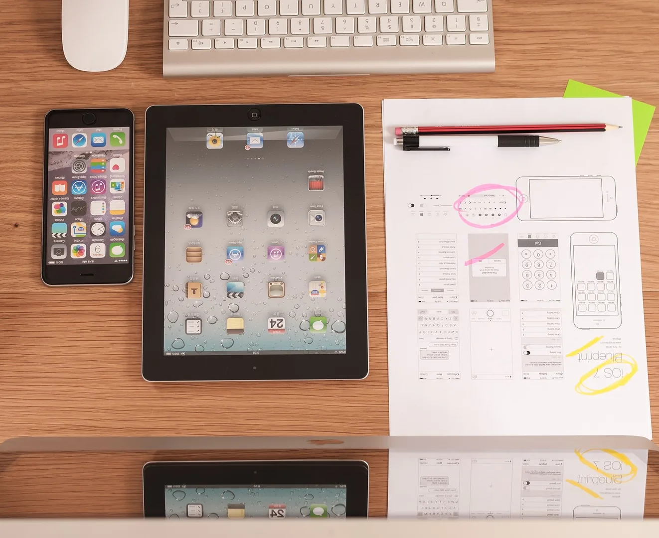 Arbeitsplatz für UX Design mit iPhone, iPad und handgezeichneten iOS-Wireframes neben Tastatur und Stiften