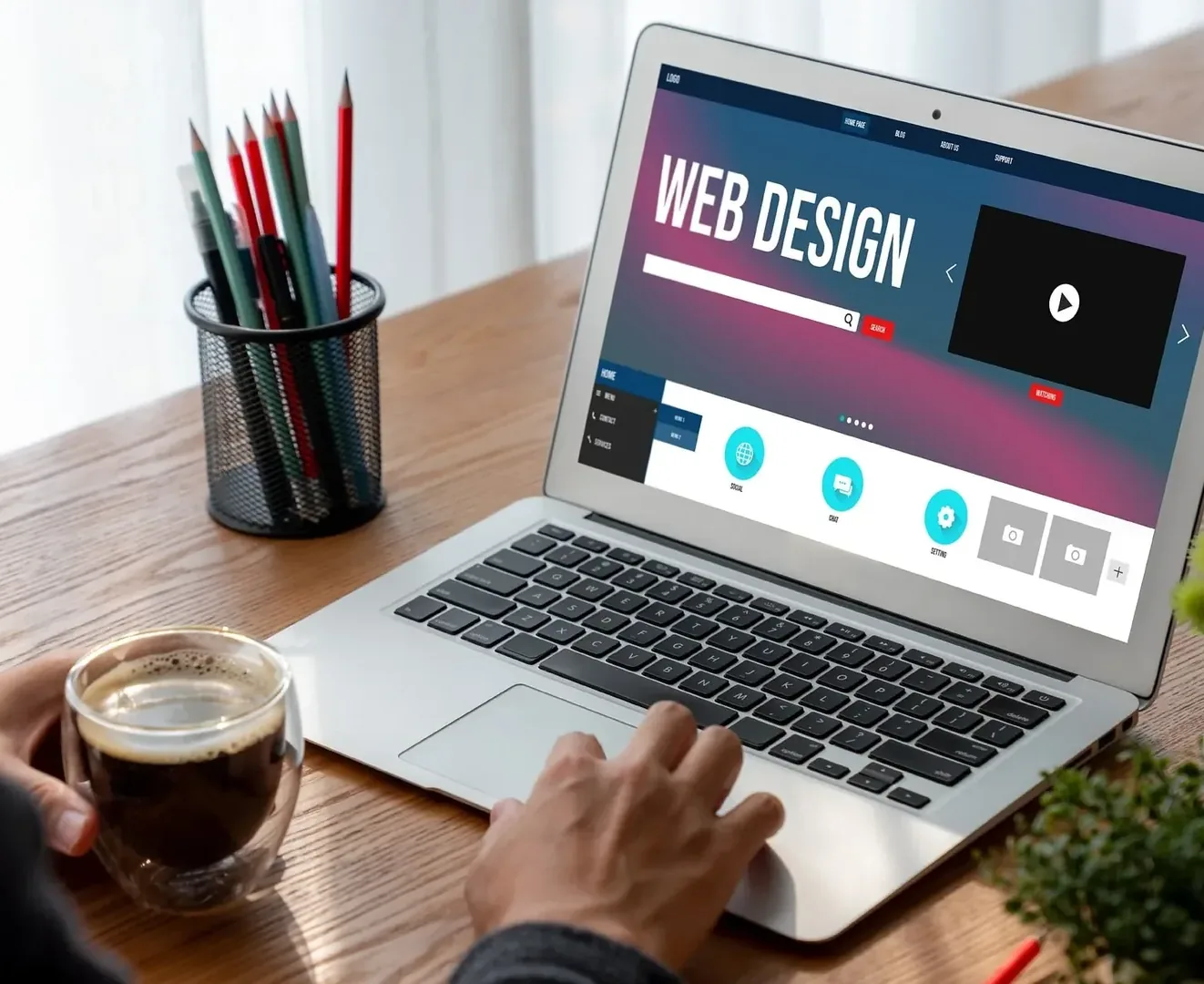 Laptop mit geöffneter Webdesign-Website auf einem Schreibtisch neben Stiften und Kaffee