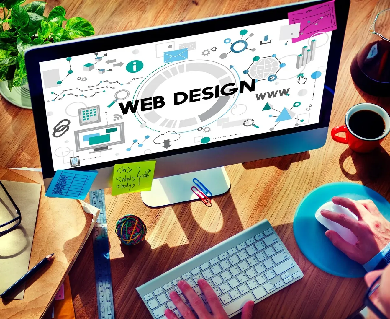 Monitor mit Webdesign-Grafik, HTML-Code und Arbeitsmaterialien auf einem Schreibtisch