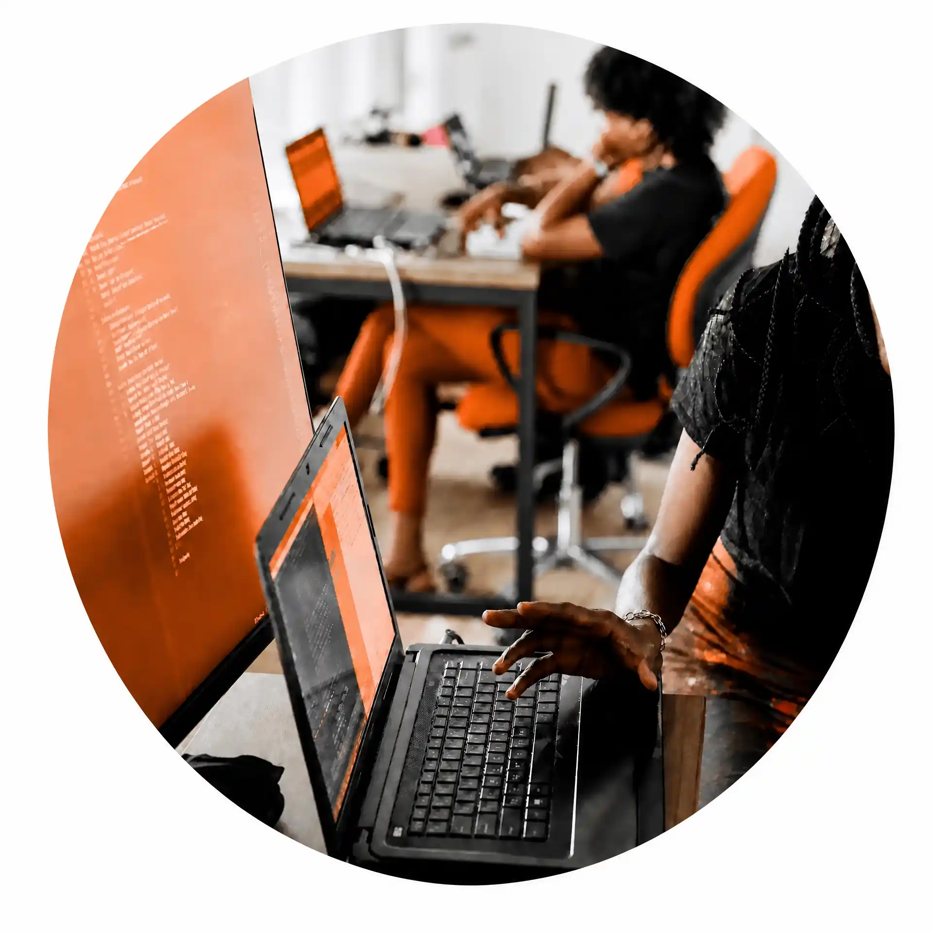Person arbeitet an einem Laptop, während ein Team im Hintergrund gemeinsam in einem modernen Büro arbeitet