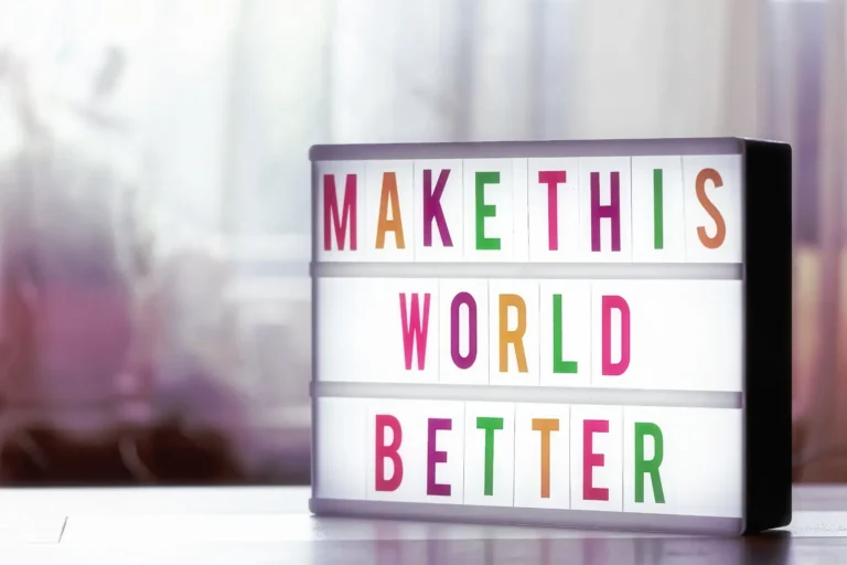 Bunter Leuchtkasten mit dem englischen Motivationsspruch „Make This World Better“ auf einem Tisch